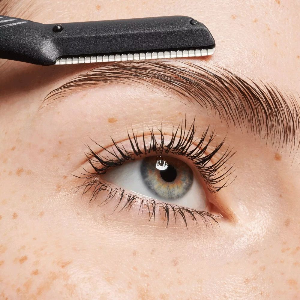 Gros plan sur un œil et un sourcil. Un rasoir à sourcils est utilisé. Manche noir, lame argentée.