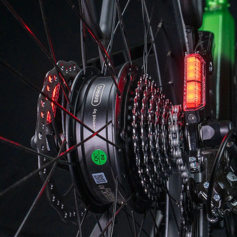 Gros plan de la roue arrière. Réflecteurs rouges, frein à disque et chaîne. Inscription : Powered by Bafang.