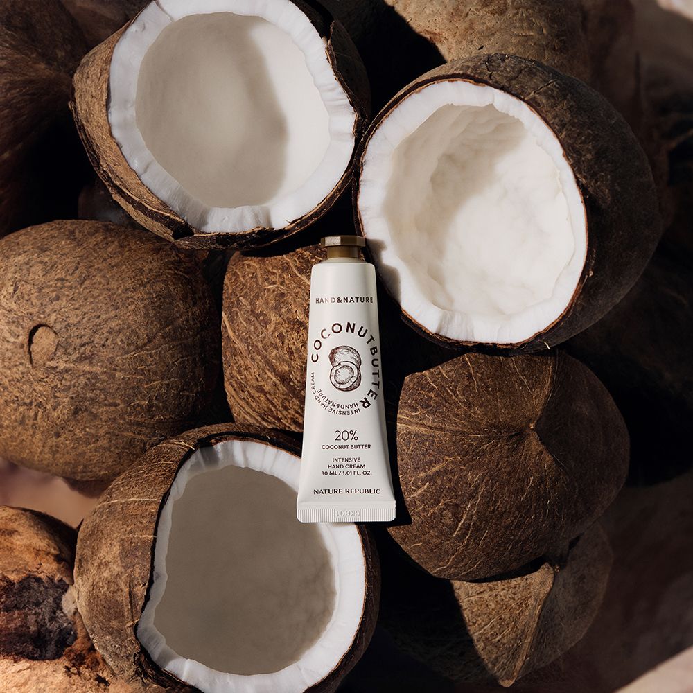 Tube de crème pour les mains sur des noix de coco. Inscription : Coconut Butter, 20% Coconut Butter, Intensive Hand Cream. Marque : NATURE REPUBLIC.