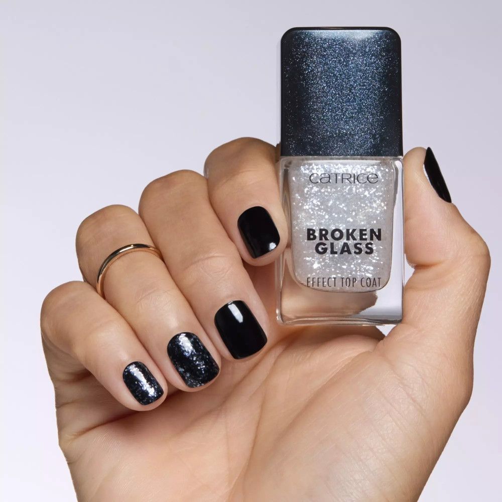 Main tenant le top coat Catrice effet verre brisé. Ongles vernis noirs, un avec paillettes.