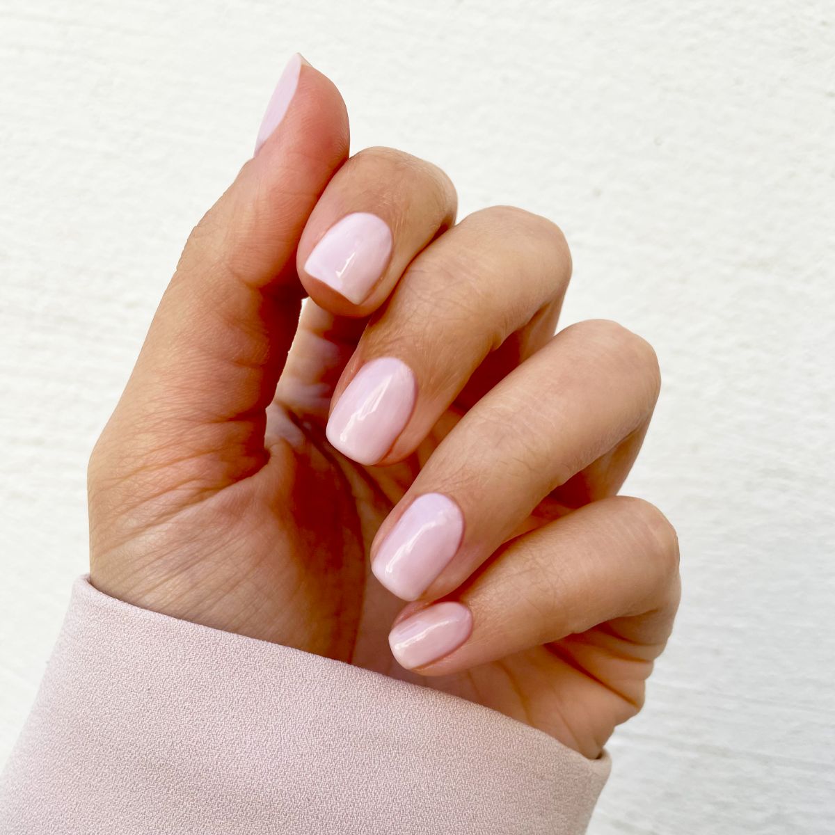 Main avec ongles vernis. Ongles rose clair. Arrière-plan: veste rose clair.