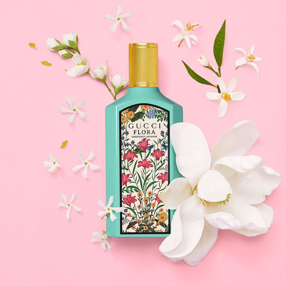 Turquoise fles met gouden dop, omringd door bloemen en bladeren. Opschrift: Gucci Flora Gorgeous Jasmine.