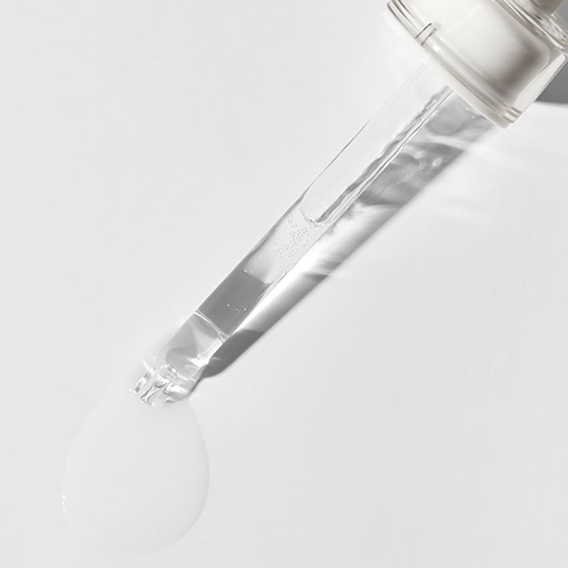 Pipet met serumdruppel. Transparante applicator met wit serum op witte achtergrond.