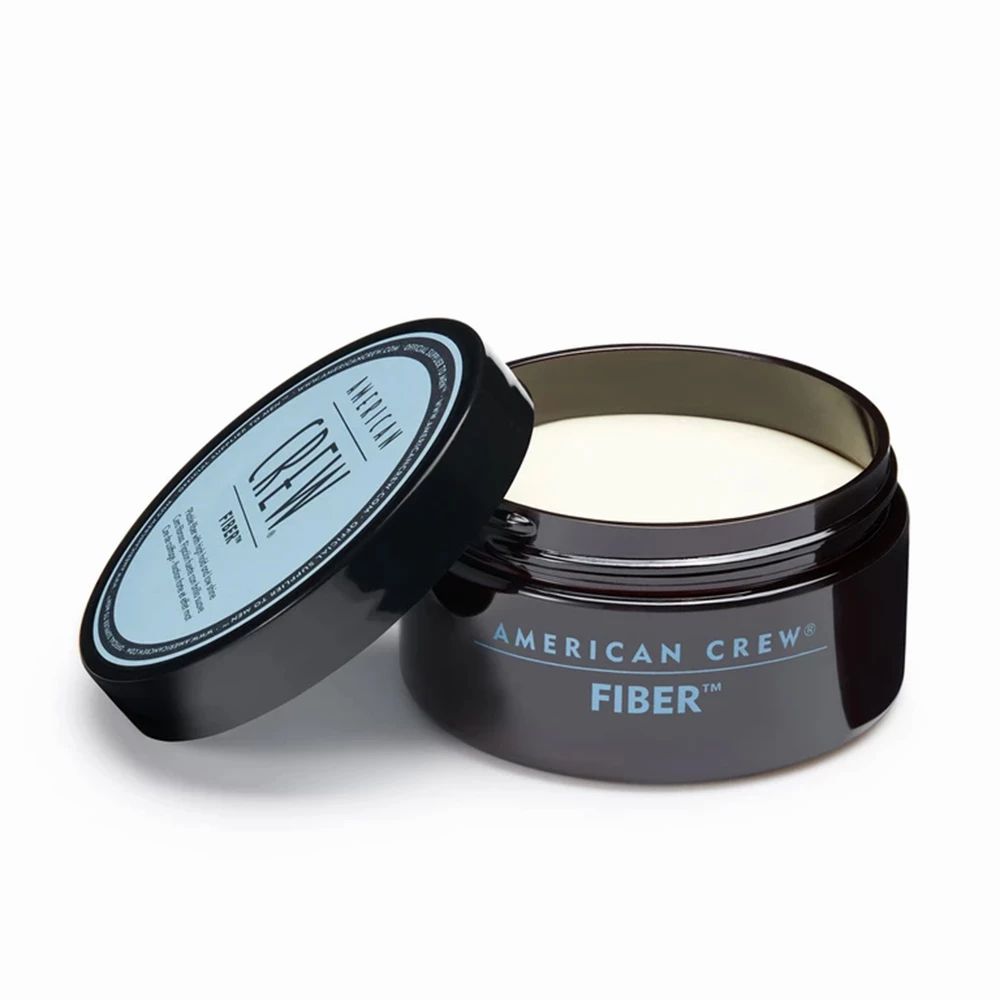 Open donkerblauwe pot met "AMERICAN CREW FIBER". Crème-kleurige haarcrème zichtbaar.