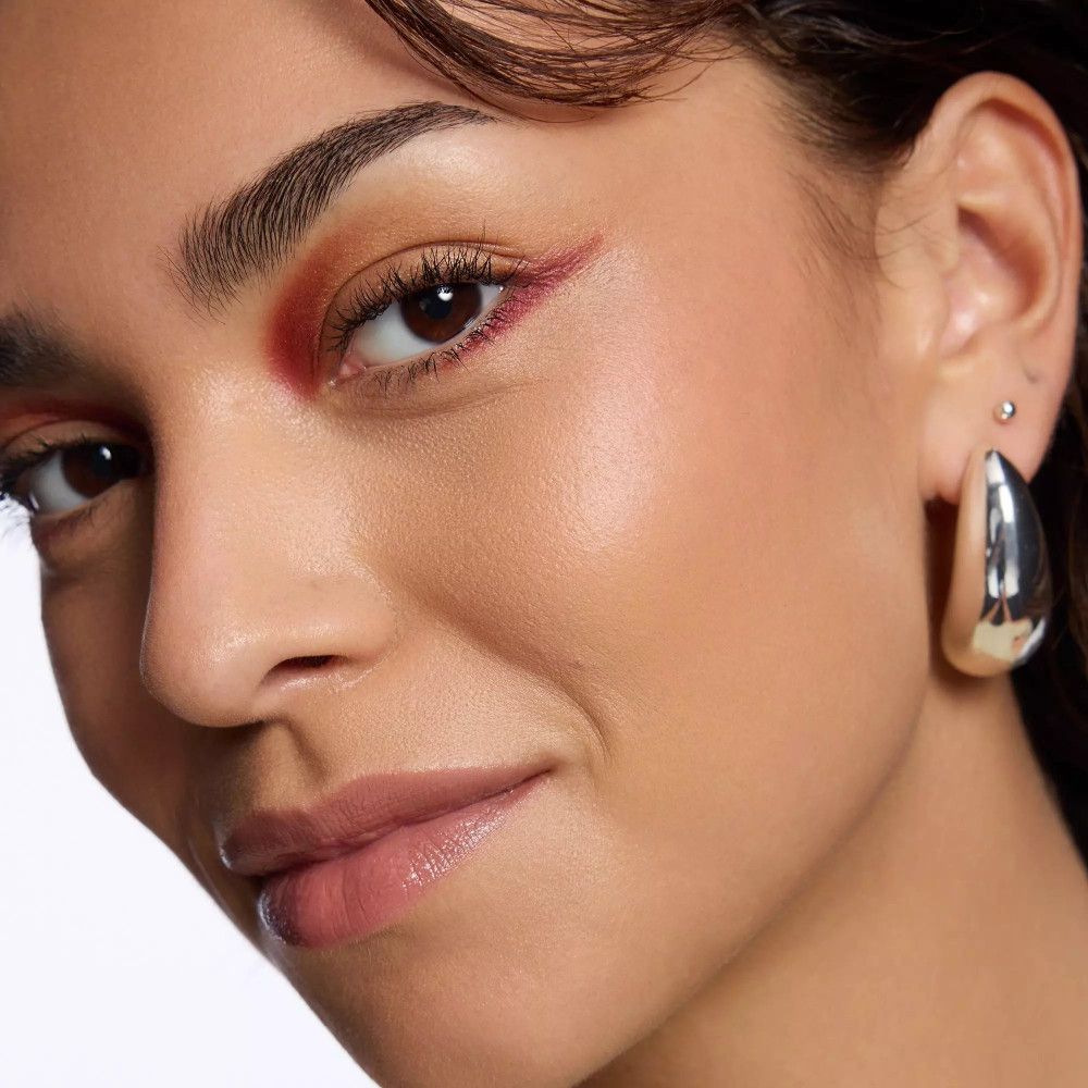 Gros plan d'une femme avec fard à paupières rose. Elle porte des boucles d'oreilles argentées.