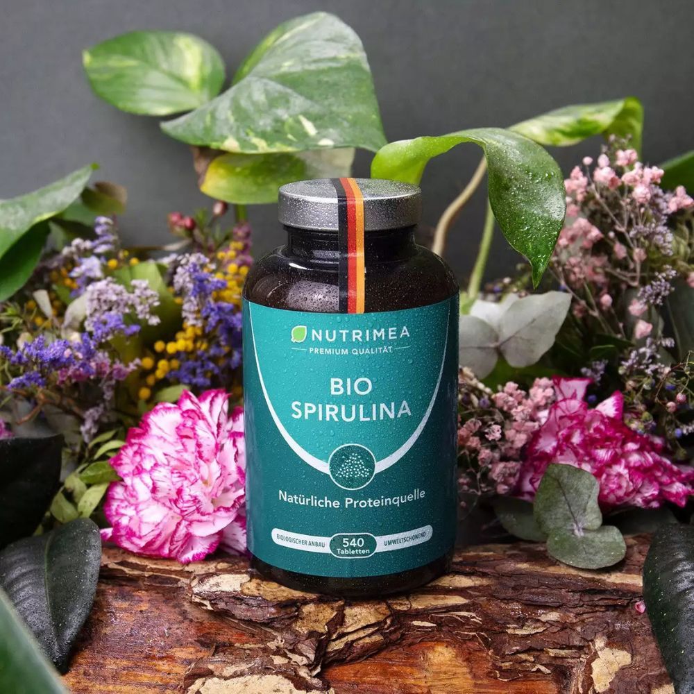Donkere fles met groene tekst BIO SPIRULINA. 540 tabletten. Natuurlijke eiwitbron. Met Duitse vlag, omringd door planten.