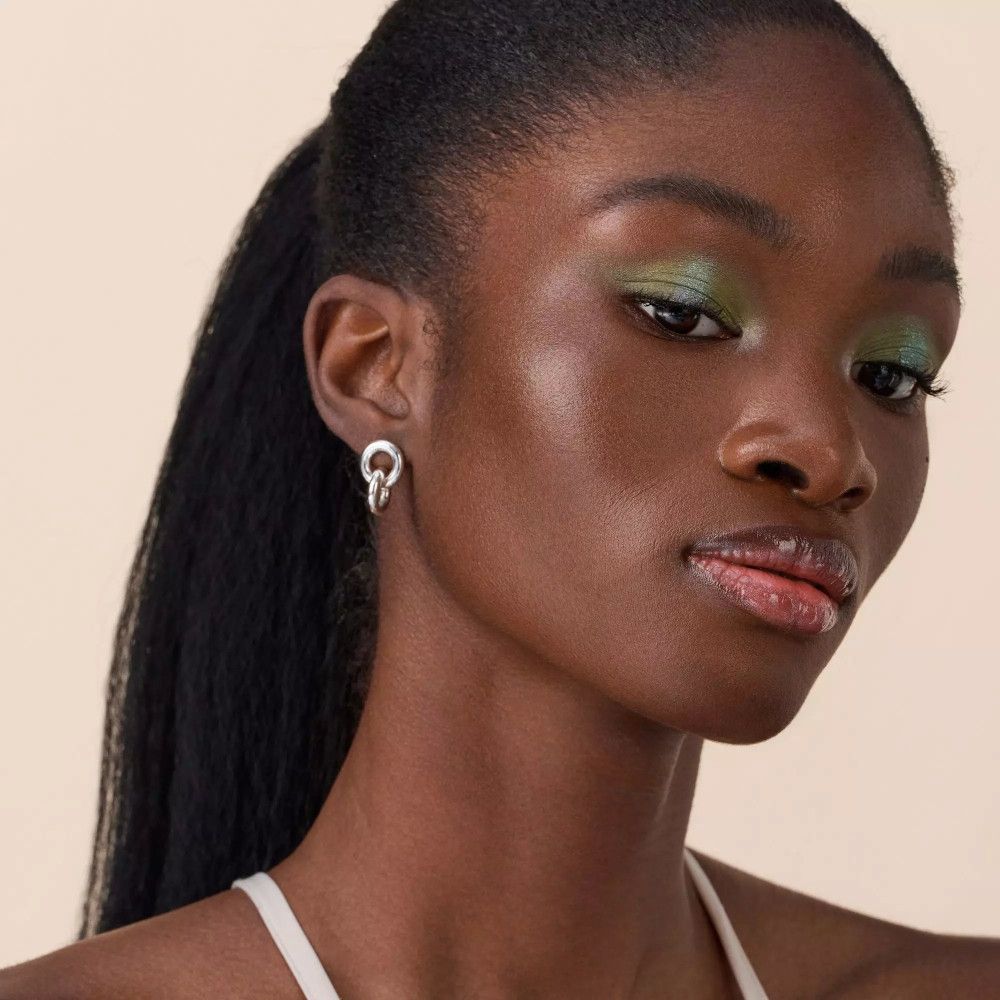 Portret van een vrouw met een donkere huid en groene oogschaduw. Ze draagt oorbellen.