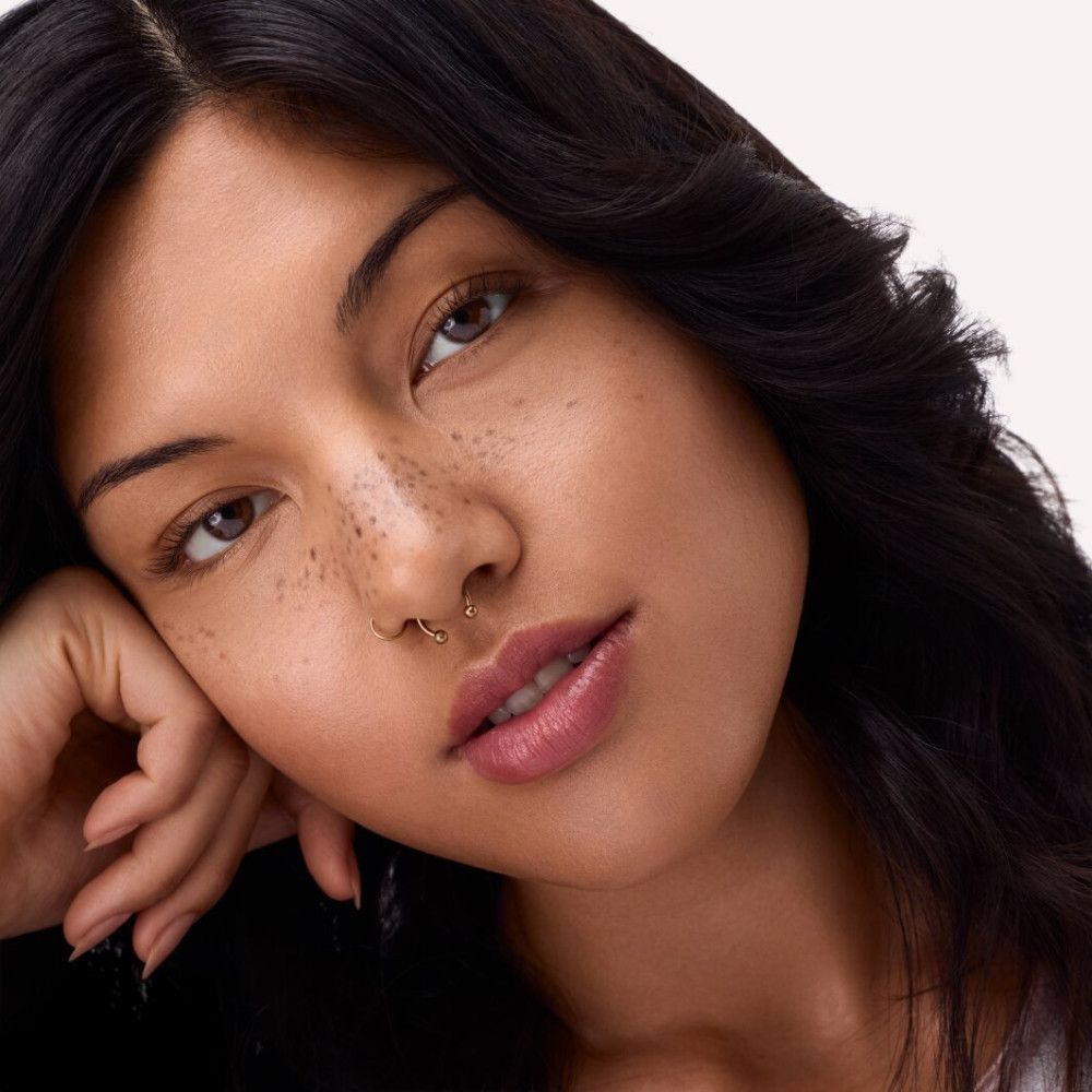 Portret van een vrouw. Vrouw met donker haar, sproeten en lippenstift. Ze steunt haar kin op haar hand.