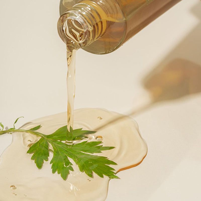 Vloeistof wordt uit een fles gegoten. Daarnaast een klodder vloeistof en een blad. Geen productaanduiding zichtbaar.