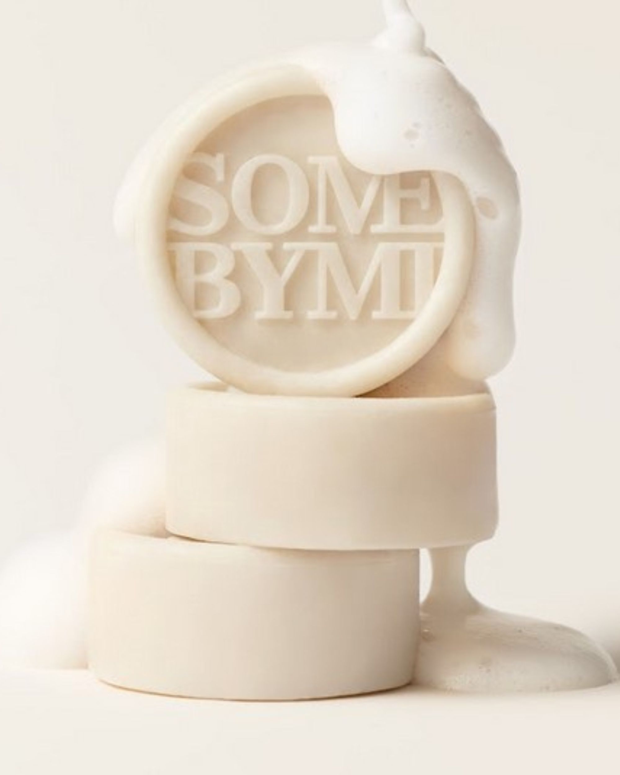 Trois savons ronds, le supérieur avec le texte SOME BYMI, recouverts de mousse. La mousse coule.