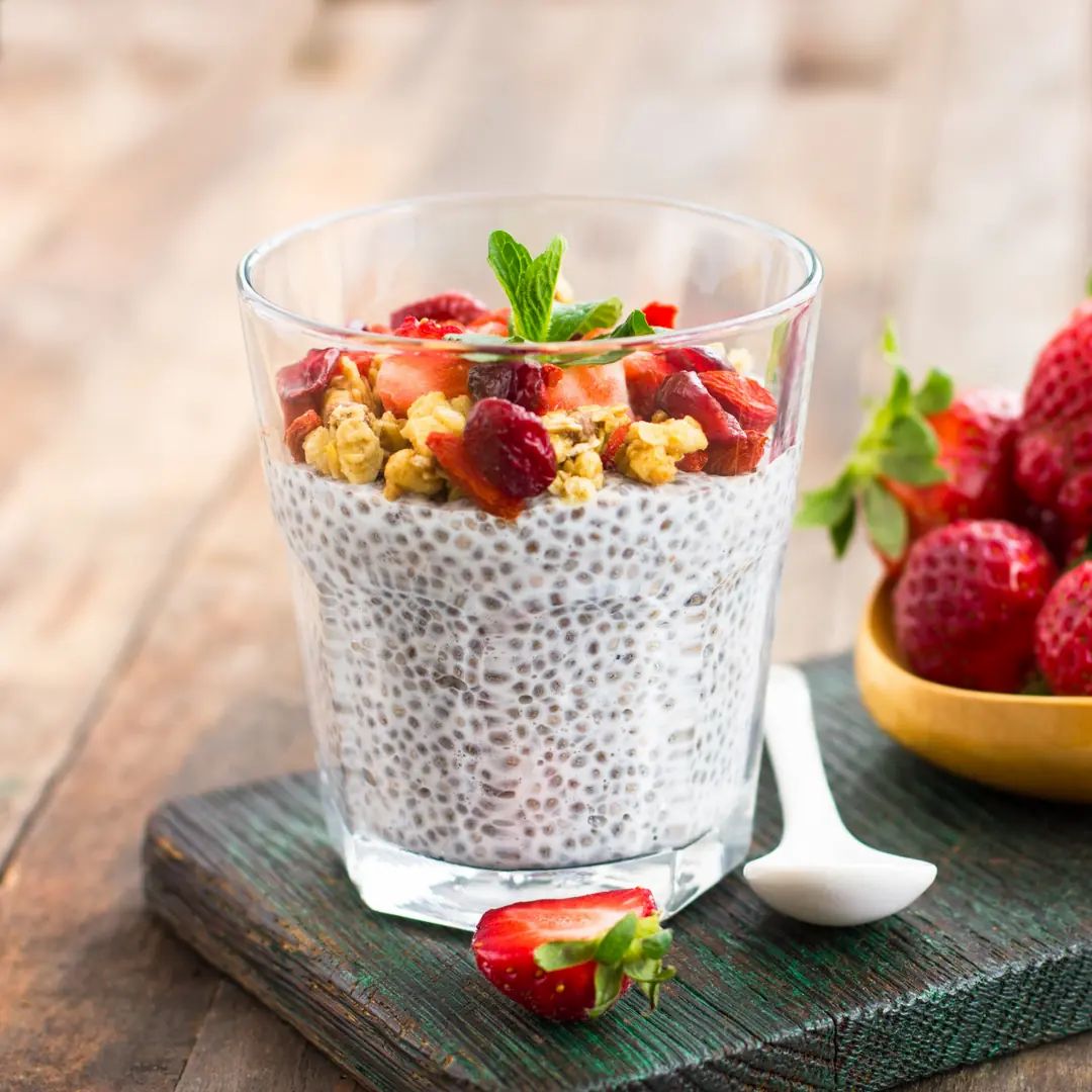Glas chia pudding, aardbeien en granola. Op een houten plank met aardbeien en lepel.