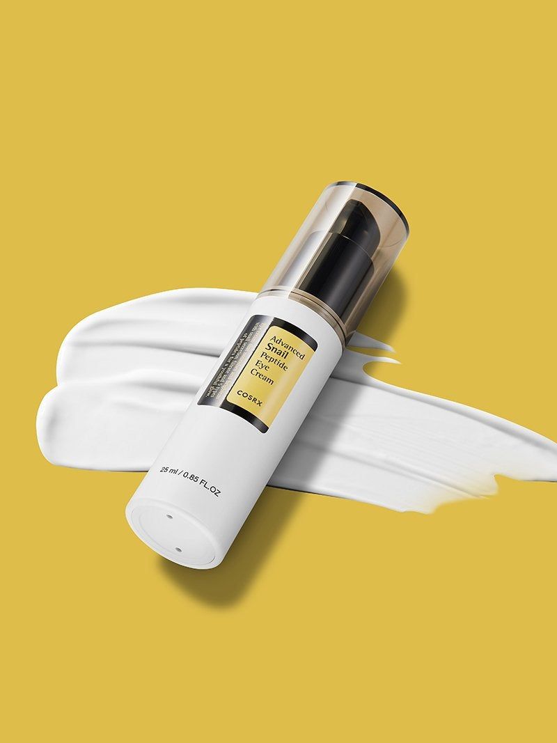 Fles op gele achtergrond met crème-uitstrijk. Zwarte pomp. Productnaam en merk zichtbaar.