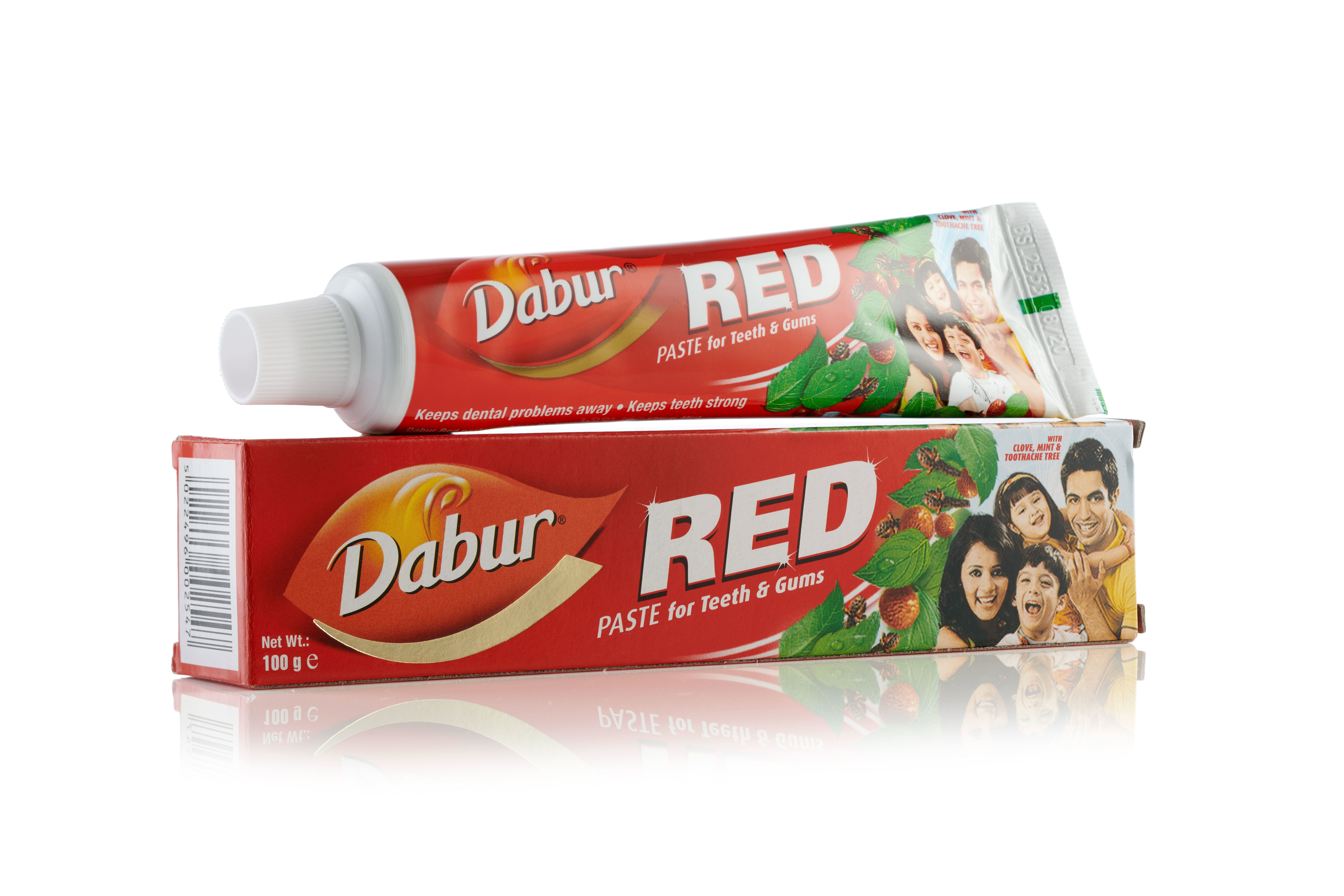 Tube de dentifrice Dabur Red posé sur son emballage rouge. Les deux montrent une image de famille.