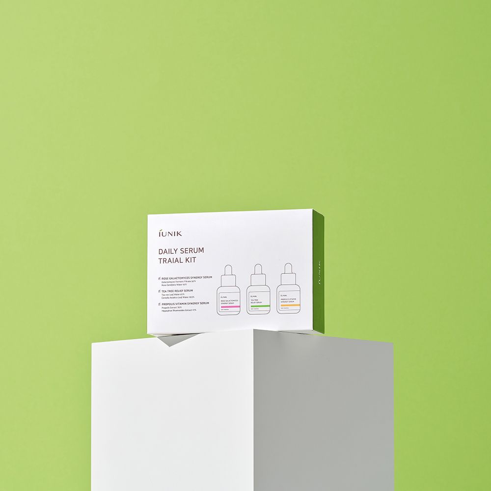 Emballage du produit sur socle blanc devant fond vert. Texte: iUNIK, Daily Serum Trial Kit. Trois illustrations de sérums.