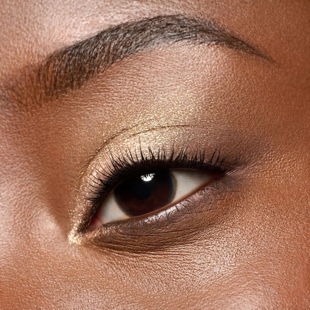 Gros plan sur un œil avec fard à paupières doré. Cils et sourcils foncés.