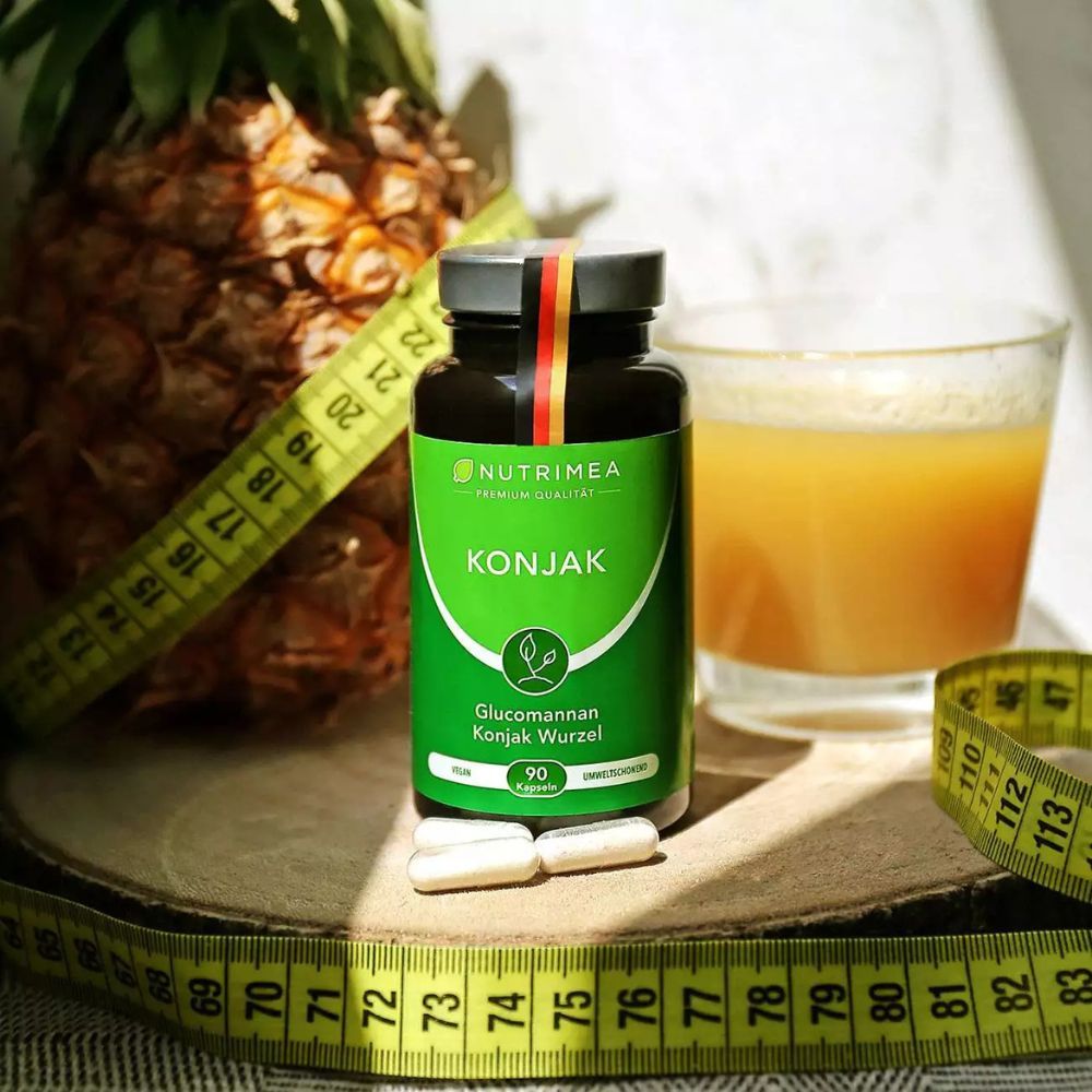 Fles KONJAK, daarnaast capsules, ananas, meetlint en glas sap. Product op houten plank.