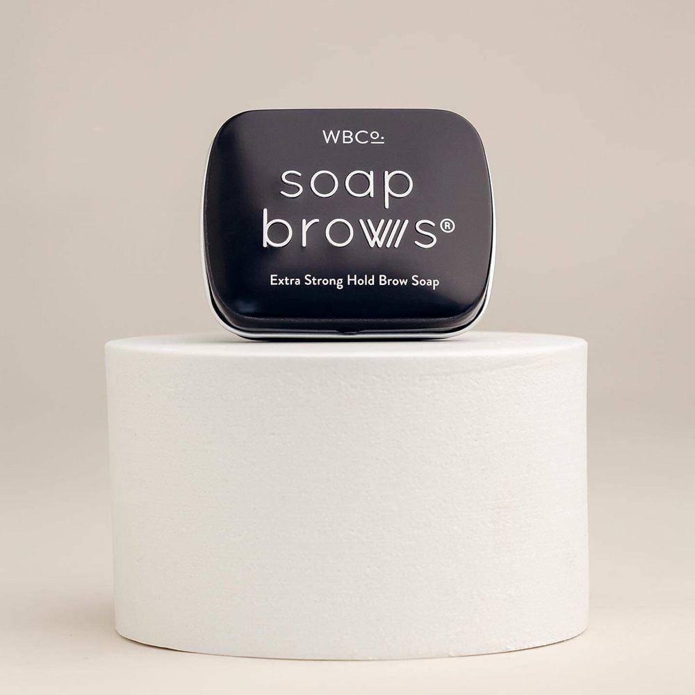 Boîte carrée noire Soap Brows sur un piédestal blanc. Nom du produit et 'Extra Strong Hold Brow Soap' visibles.