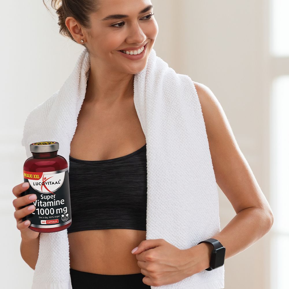 Vrouw houdt fles Super Vitamine C vast. Draagt sportkleding en handdoek. Merk Lucovitaal.