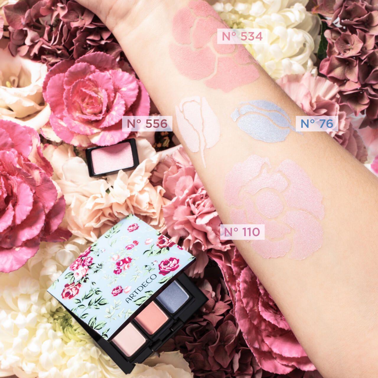 Arm met verschillende oogschaduwkleuren. Artdeco palet met vier kleuren. Bloemen op de achtergrond. Kleurnummers op de arm.