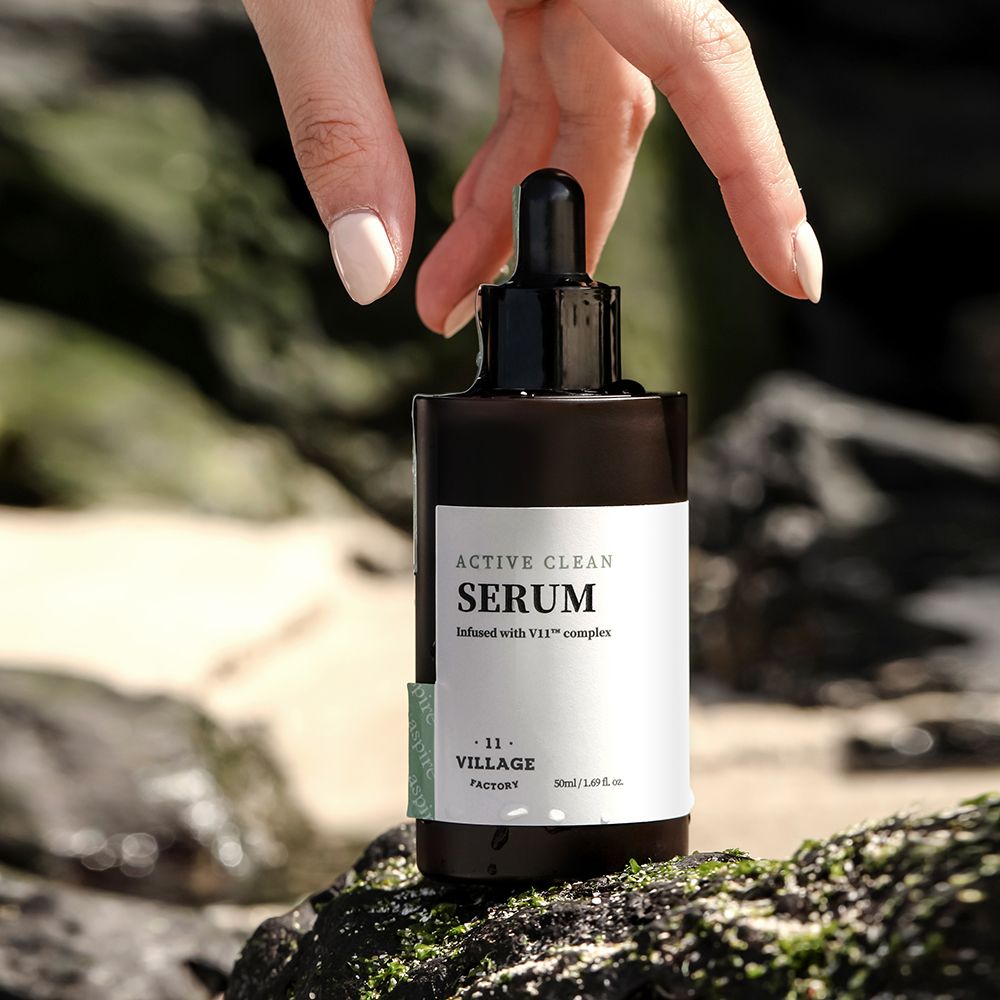 Bruine serumfles met zwarte dop en pipet, vastgehouden door een hand. Op rotsen.