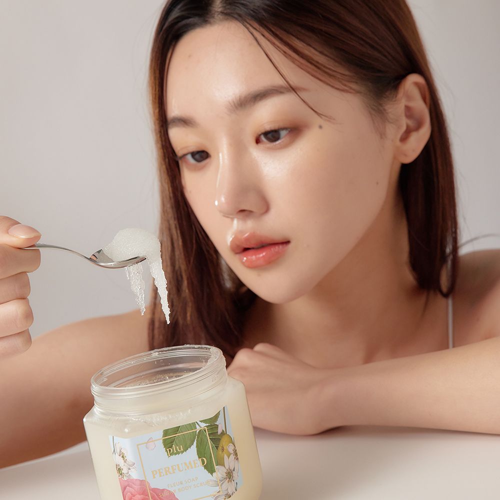 Femme tenant une cuillère avec gommage corporel. Pot en verre avec couvercle doré et étiquette au design floral.