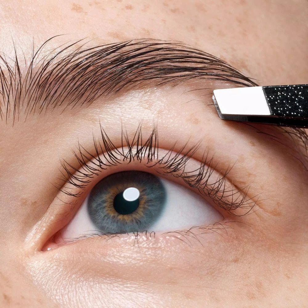 Close-up van een oog. Een pincet plukt wenkbrauwhaartjes. Zwarte pincet met zilveren punt.