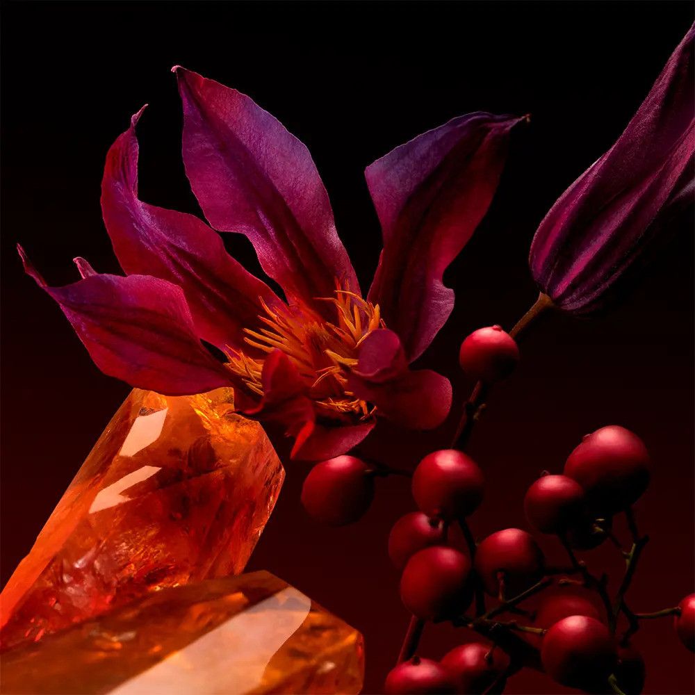 Close-up van een bloem met rode bessen en een oranje kristal tegen een donkere achtergrond.