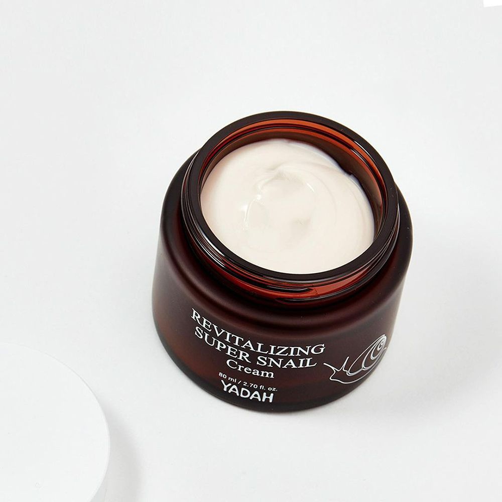 Pot de crème brun ouvert avec crème blanche. Inscription: Revitalizing Super Snail Cream, YADAH. Illustration d'escargot.