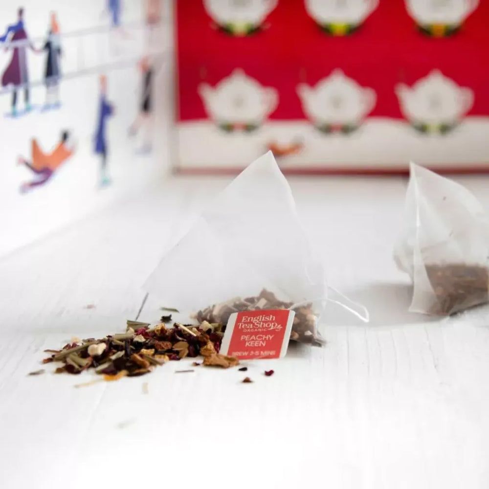 Sachets de thé pyramide ouverts avec feuilles de thé en vrac. Étiquette rouge avec logo et texte English Tea Shop. Sur fond blanc.