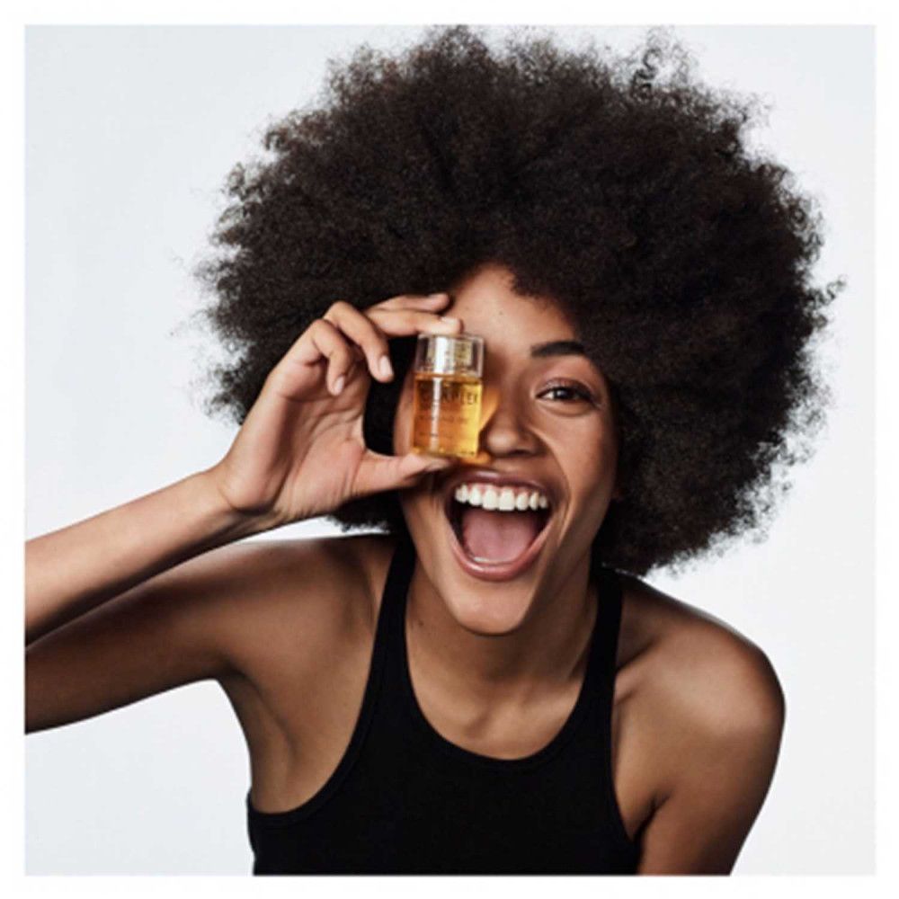 Vrouw houdt Olaplex No.7 Bonding Oil voor haar oog. Ze lacht. Het product zit in een kleine fles.