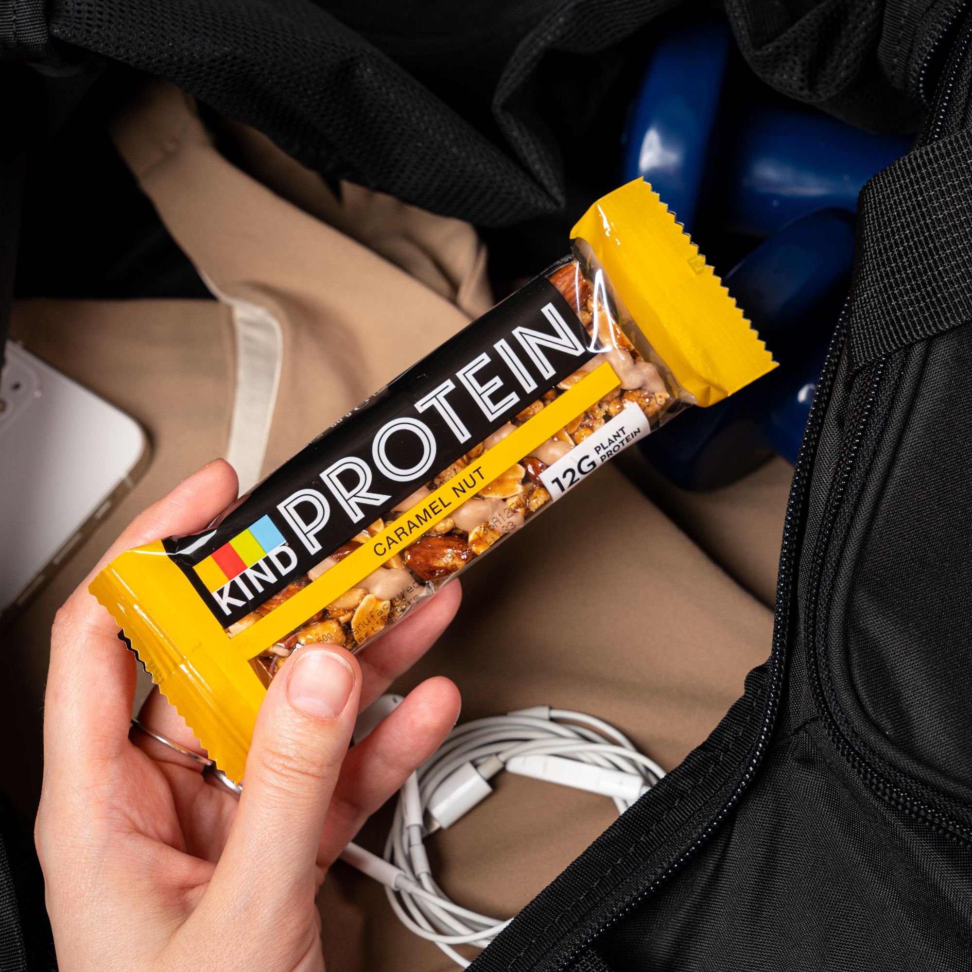 Hand houdt verpakte eiwitreep vast. Opschrift: BE-KIND, PROTEIN, 12G PLANT PROTEIN, Caramel Nut.