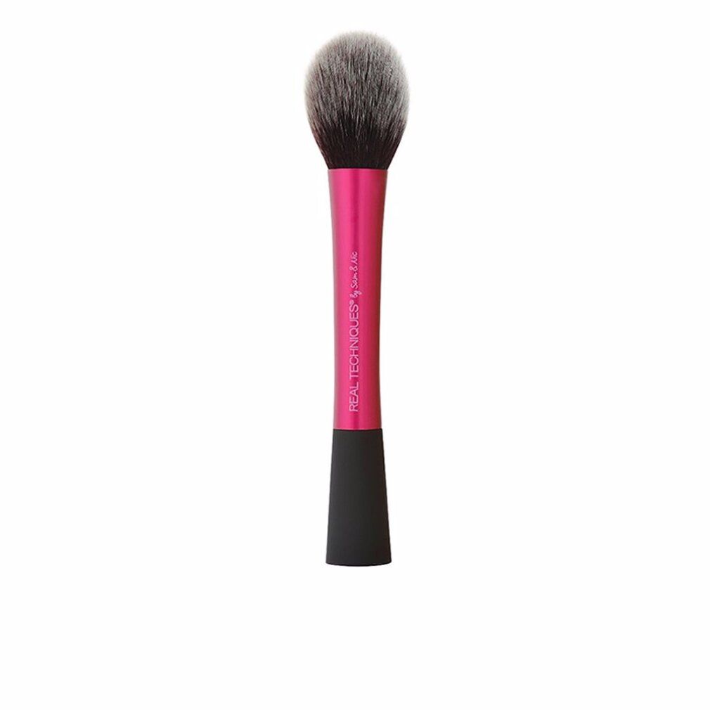 Pinceau à poudre avec manche rose et poils gris-noirs. "REAL TECHNIQUES" est écrit sur le manche.