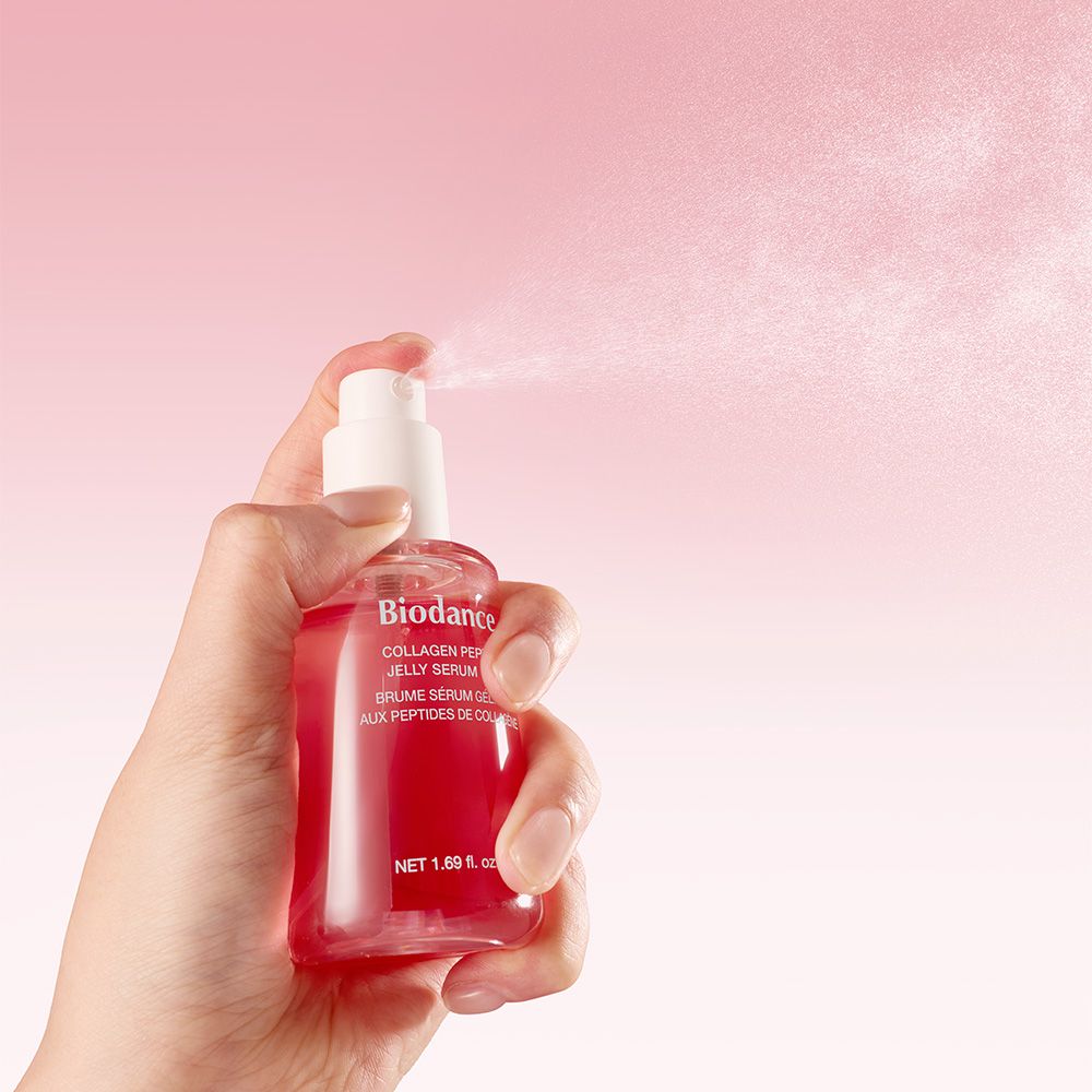 Hand houdt een spuitfles met rood serum vast. De spuitkop vernevelt fijne druppeltjes.