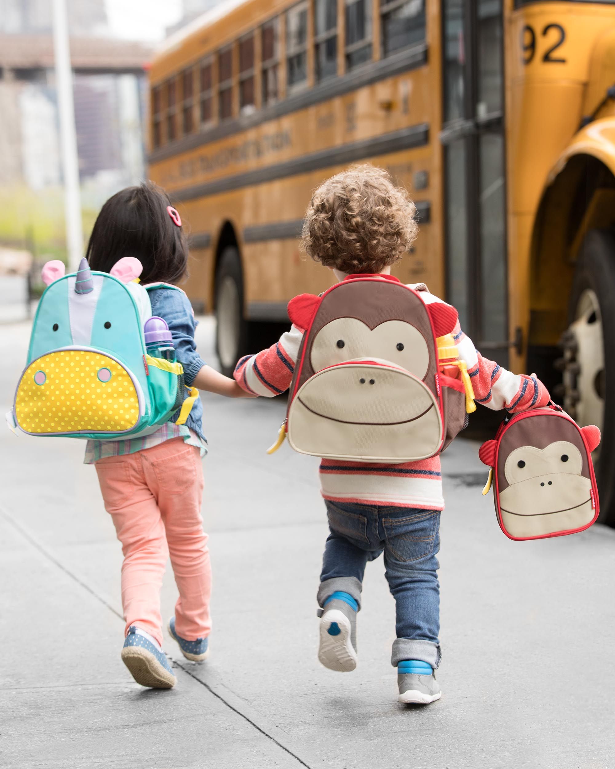 Twee kinderen lopen naar school met rugzakken. Een met een eenhoornrugzak, de ander met een apenrugzak.