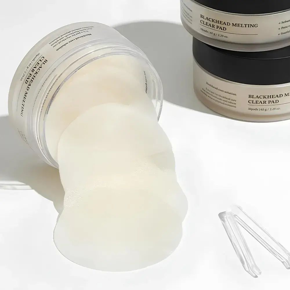 Pot ouvert avec pads. Pads sortent. Une pince à épiler à côté. Autres pots en arrière-plan.