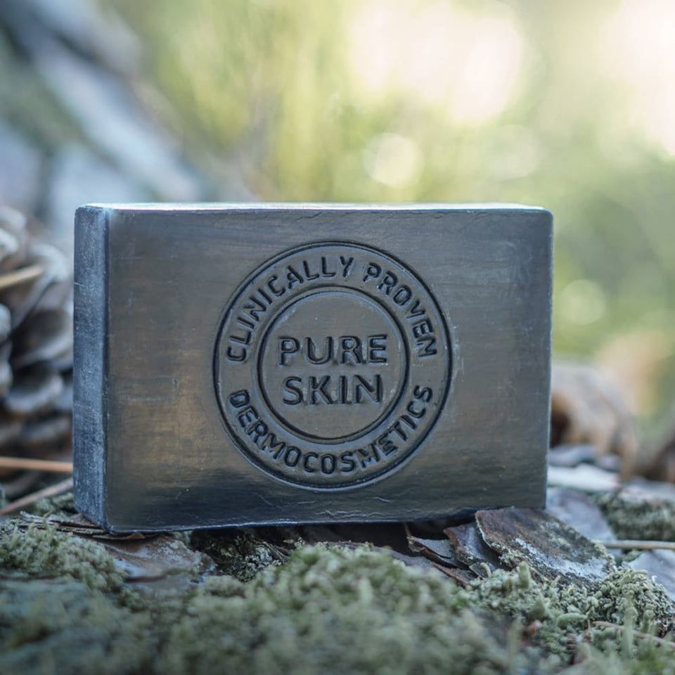 Rechthoekige zwarte zeep met reliëf. Op mos en dennennaalden. Tekst: Clinically Proven, Pure Skin.