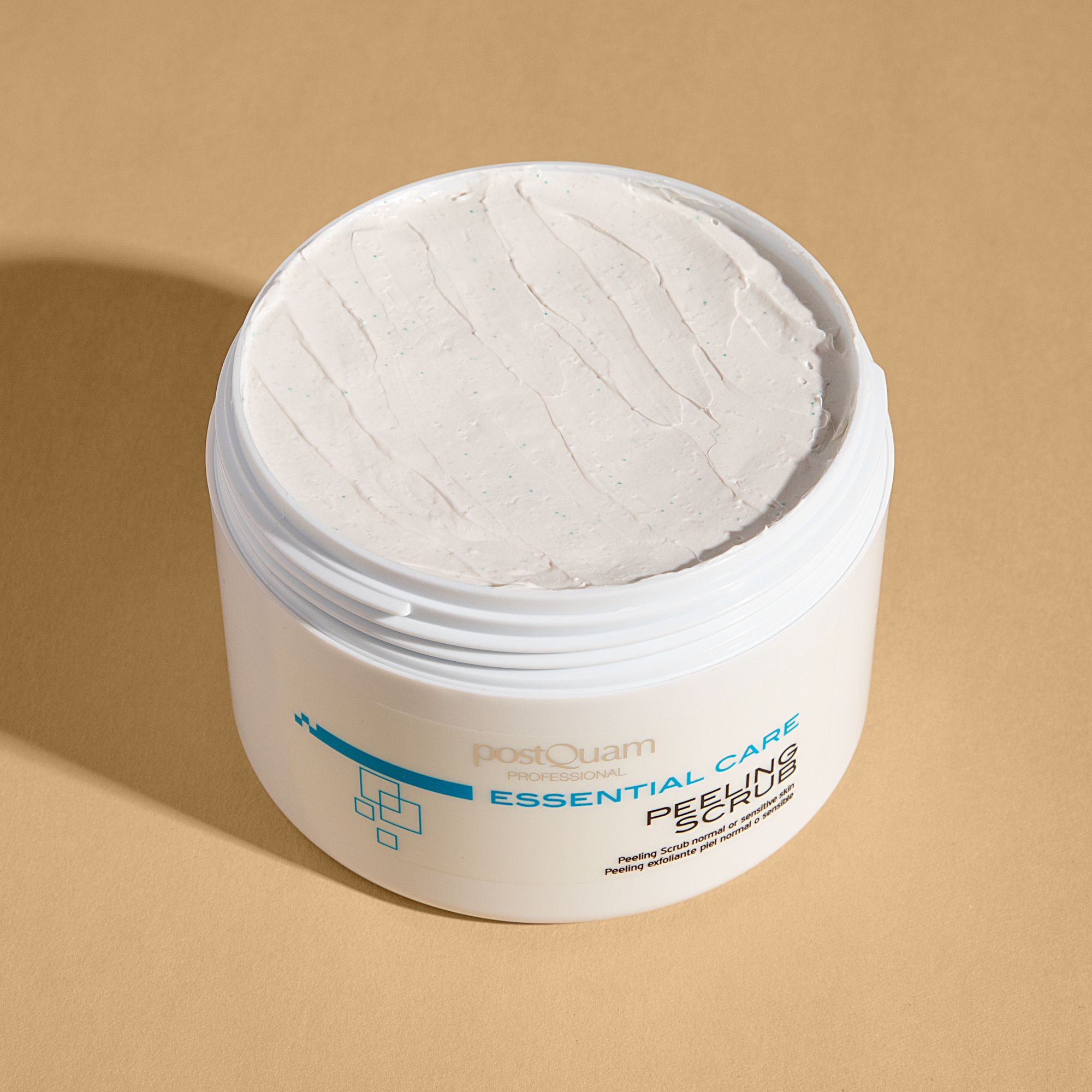 Witte pot, open, met crème-achtige substantie. Opschrift: Essential Care Peeling Scrub. Voor normale of gevoelige huid.
