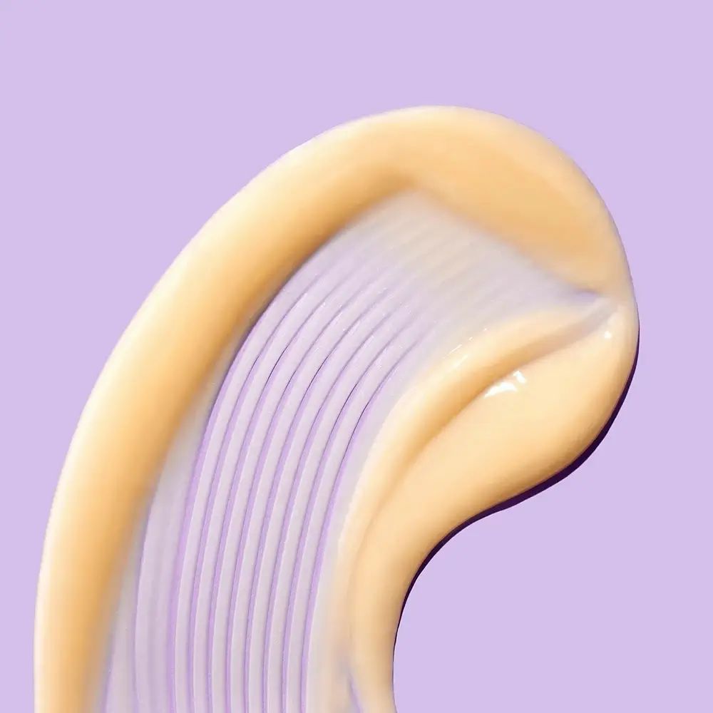 Close-up van een crèmekleurig product op paarse achtergrond. Product met geribbelde textuur. Glanzend oppervlak.