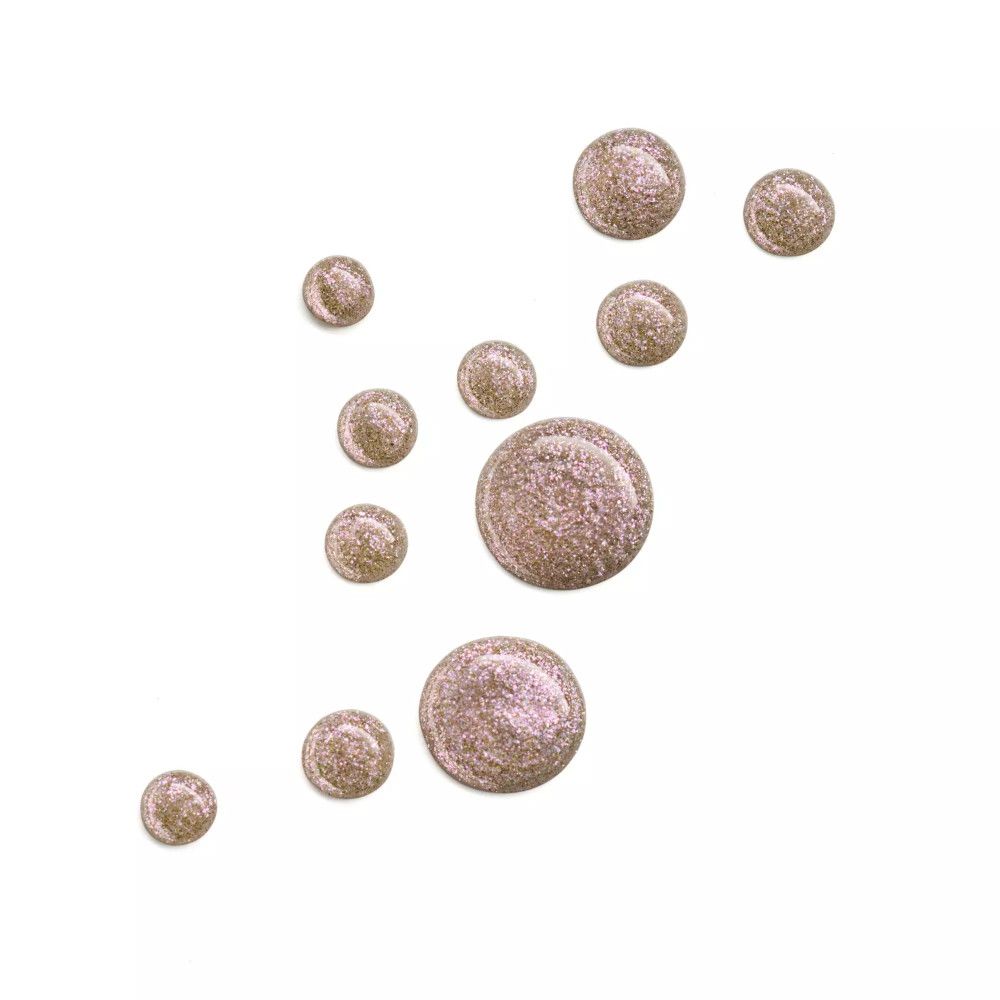 Plusieurs gouttes de vernis à ongles rose pailleté sur fond blanc.