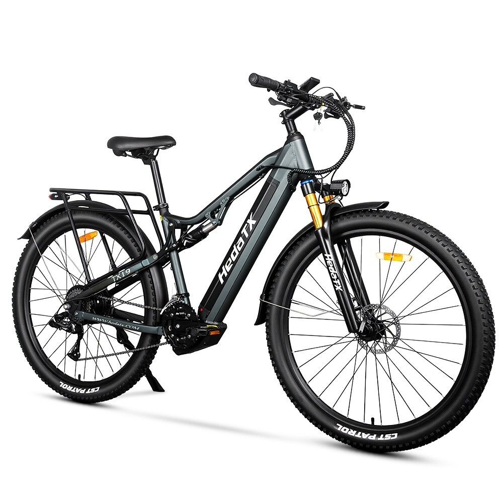 Vélo électrique gris HedaTX TX19. Pneus noirs, porte-bagages, suspension. Fourche jaune. 27 vitesses. Inscription HedaTX.