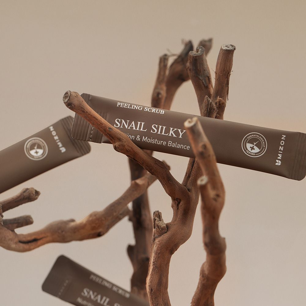Meerdere individuele verpakkingen op takken. Opschrift: PEELING SCRUB, Snail Silky, MIZON. Bruine kleuren.