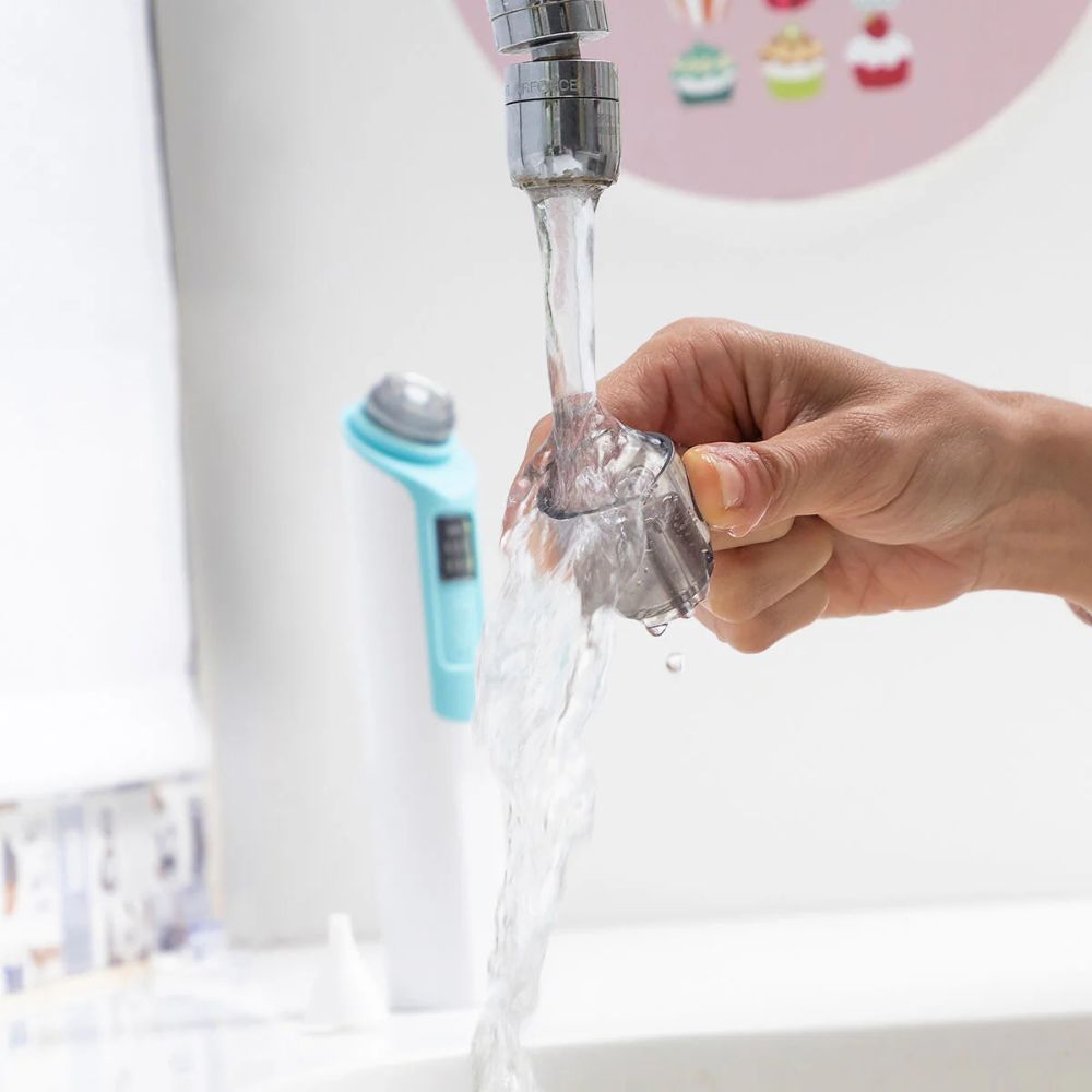 Neusaspiratoropzetstuk onder stromend water. Het opzetstuk is transparant. De rest van het apparaat is blauw.