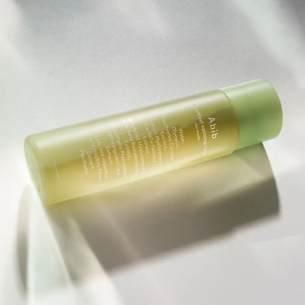 Groene fles met witte tekst. Opschrift: Abib Heartleaf calming toner Skin Booster. Ligt op een oppervlak.