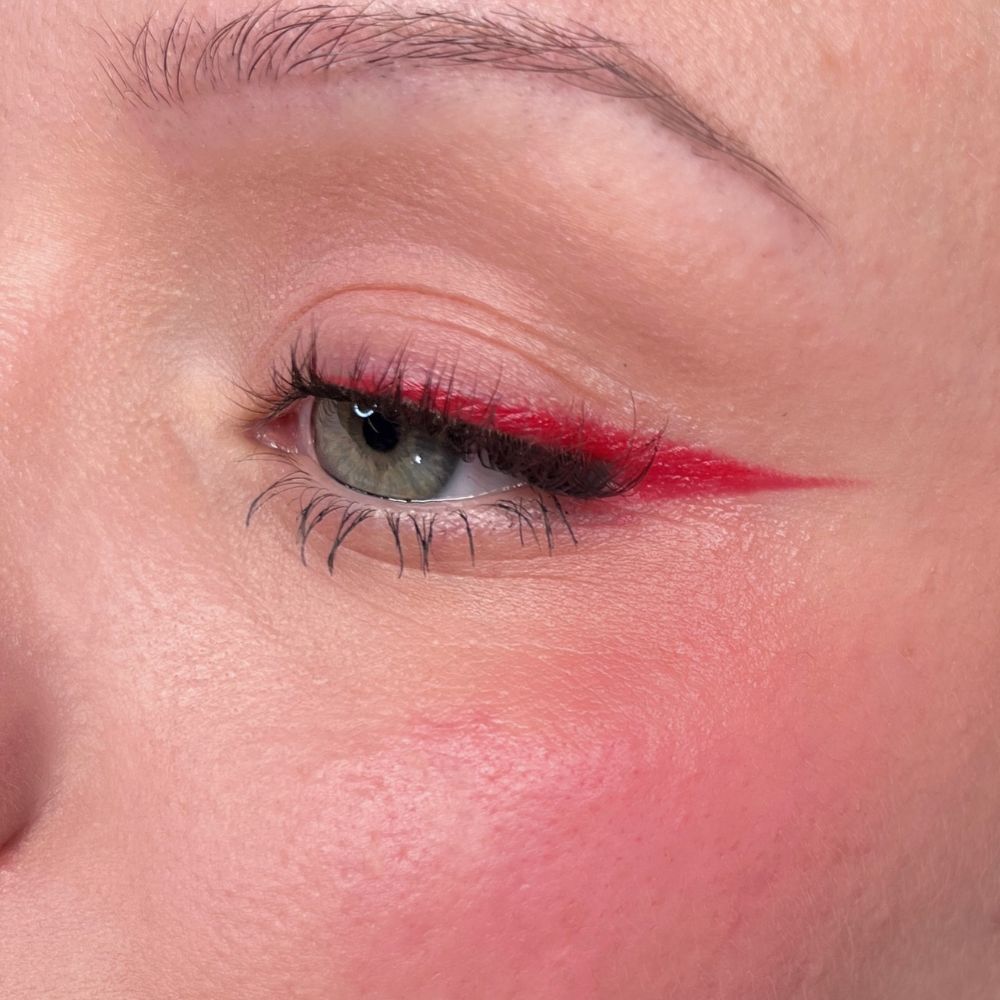 Close-up van een oog met rode eyeliner en blush. Groen oog. Product: ALL TIGERS.