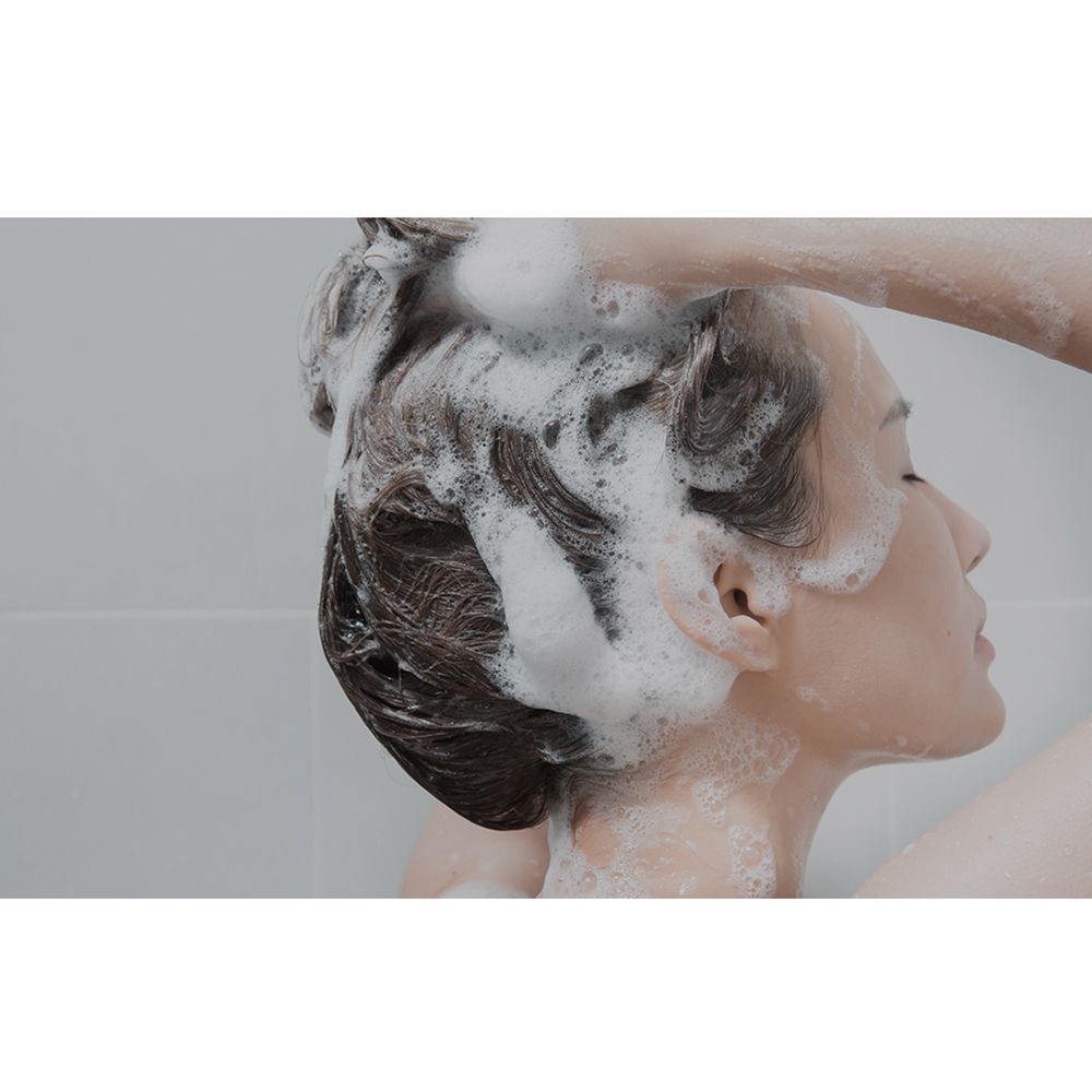 Persoon wast haar met shampoo. Hoofd en haar bedekt met schuim.