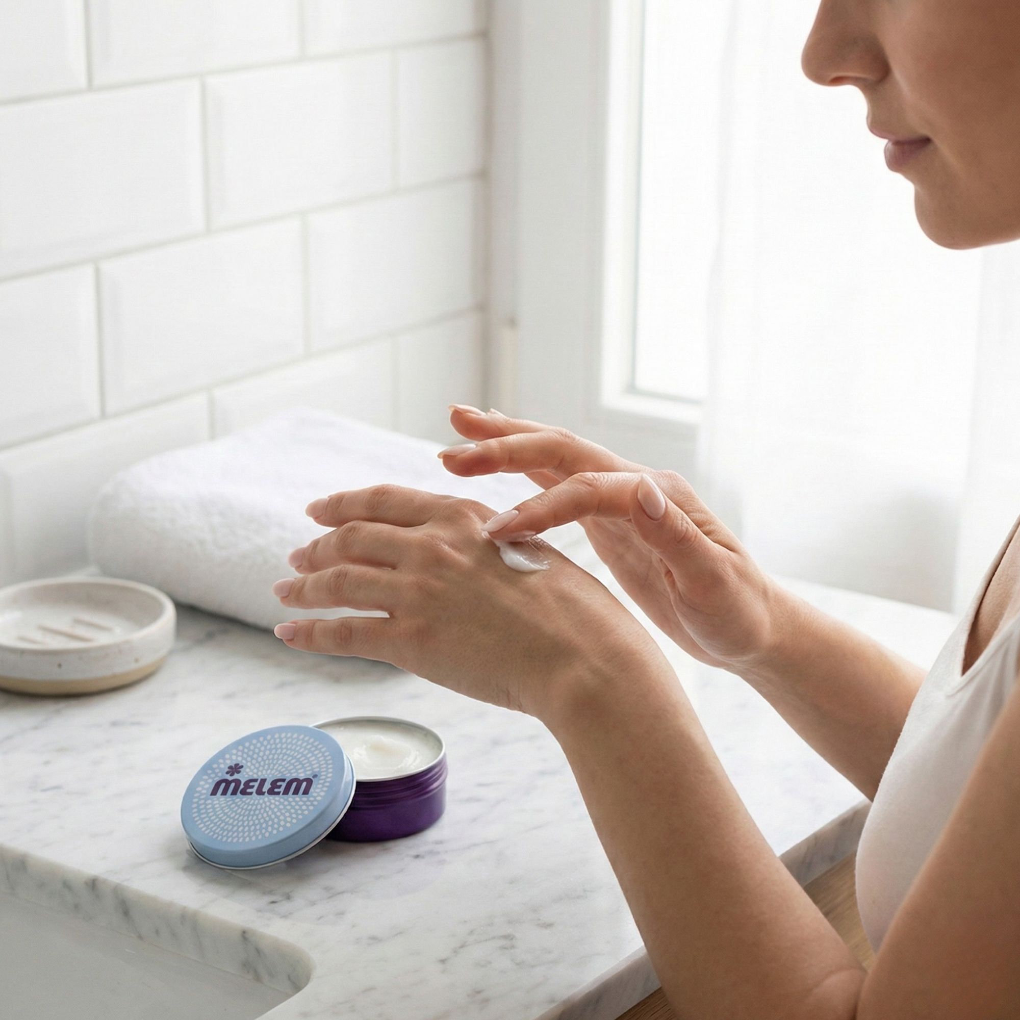 Persoon brengt crème aan. Open, ronde pot met "MELEM" logo. Pot staat naast een persoon die crème op de hand aanbrengt.