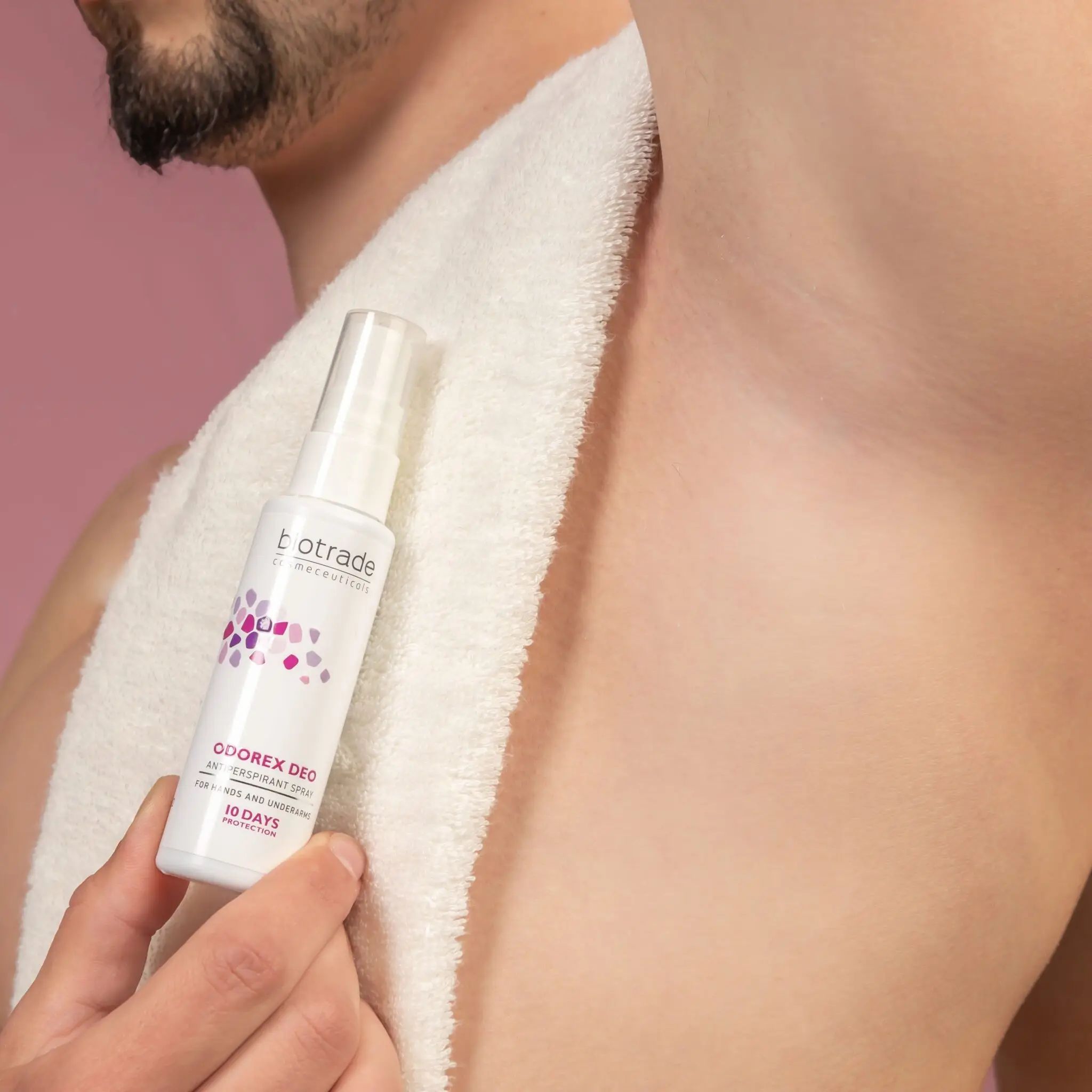 Wit spray met tekst. Gehouden onder de arm van een man. Handdoek op de achtergrond. Roze achtergrond.