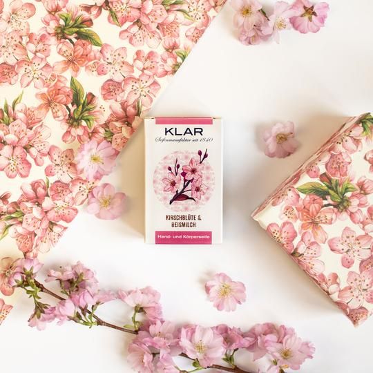 Klar zeepverpakking en cadeaupapier met kersenbloesemmotief. Verpakking: wit met roze accenten. Opschrift: Kirschblüte & Reismilch, hand- en lichaamszeep.