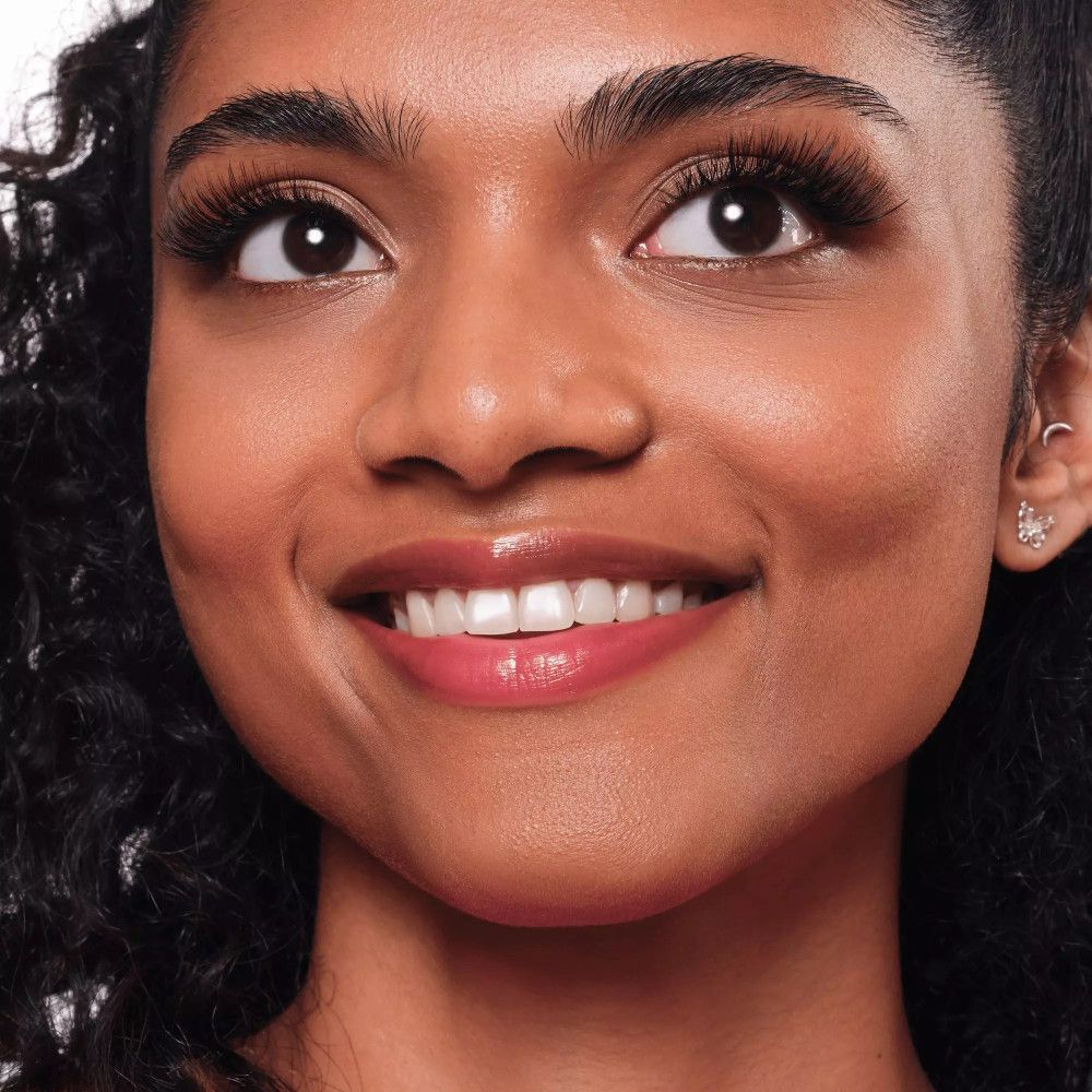 Gros plan d'une femme avec de faux cils. Peau foncée, yeux bruns, souriante.