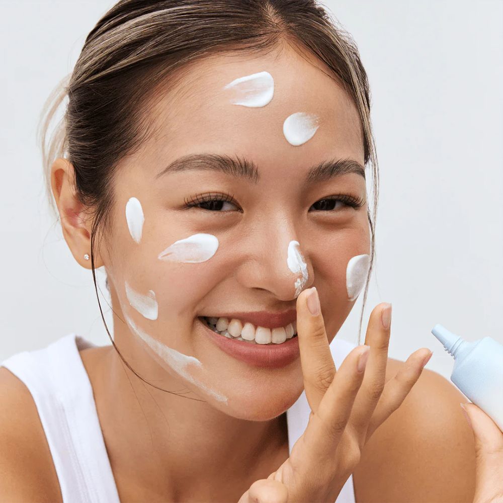 Femme appliquant une crème solaire blanche sur son visage, tenant un tube.